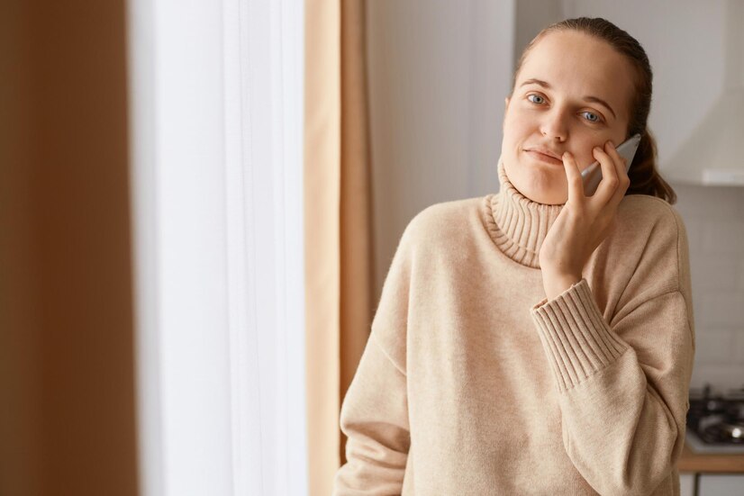 image helpless confused woman wearing beige sweater posing near window talking cell phone being sure what answer shrugging shoulders looking camera 176532 18732